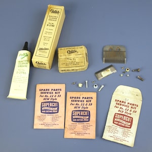 May include: An assortment of vintage Oster electric clipper parts and accessories, including a tube of clipper grease, boxes, service kits, and clipper blades. The items are arranged on a blue surface.