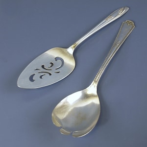 May include: Two silver serving utensils: a pie server with a decorative cut-out design and a serving spoon. Both pieces have long, slender handles with floral detailing at the ends. The pie server is approximately 9 inches long, and the spoon is about 8 inches long.