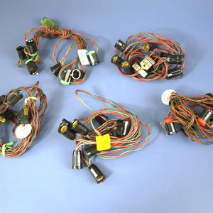 May include: A collection of vintage Christmas light strings. Each string features black bulb sockets with red, green, and gold wiring. Some strings are bundled with rubber bands and tags, set against a blue background.