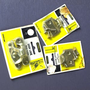 May include: Three packages of Stanley brand hardware for windows. The packages are yellow with black text and contain brass plated sash locks and hook lifts. The packages include screws.