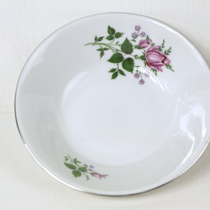May include: A white ceramic bowl with a silver rim and a floral design featuring pink roses and green leaves.