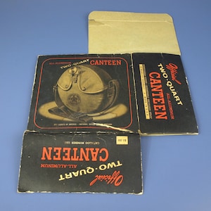 Puede incluir: Una caja de cartón negra y roja con el texto "Official Two Quart All-Aluminum Canteen" y una imagen de una cantina verde con el logotipo de Boy Scouts of America. La caja tiene un precio de $ 3.00 y el número de catálogo 1200.