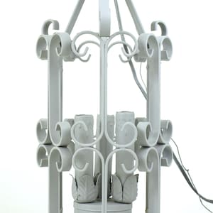 May include: A gray metal candle lantern with a decorative, scrollwork design. The lantern has a rectangular shape with curved accents and a central support for candles. It features a top handle and a base with leaf-shaped details.