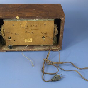 Puede incluir: La parte posterior de una radio vintage de madera con un cable marr&oacute;n y un enchufe de dos clavijas. La radio tiene una etiqueta que dice "H 216" y "114 kc - 1150 kc".