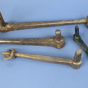 Könnte beinhalten: Vier antike Metallscharniere und ein Metallwerkzeug sind auf einer blauen Oberfläche angeordnet. Die Scharniere sind in verschiedenen Größen und haben ein rustikales, gealtertes Aussehen. Das Werkzeug ist schwarz und spitz.