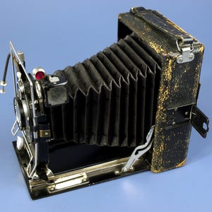 May include: A vintage black and silver folding camera with a bellows and a leather exterior. The camera has a red knob and a silver strap.