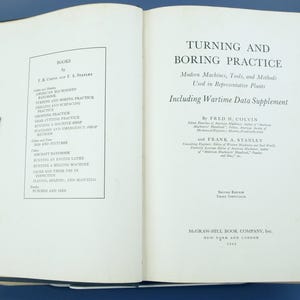 May include: Open book titled "Turning and Boring Practice" by Fred H. Colvin and Frank A. Stanley. The book's cover is black, and the pages are off-white. The text includes "Modern Machines, Tools, and Methods" and "Including Wartime Data Supplement."