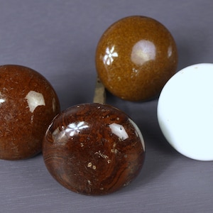 May include: Four ceramic door knobs, two brown with white flower designs, one brown with a wood grain pattern, and one white.