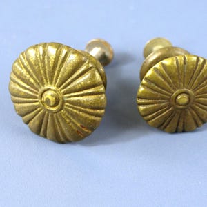 以下が含まれることがあります： 太陽の光線模様の金色の金属製のキャビネットノブが2つ。ノブは中央が盛り上がっており、滑らかで光沢のある仕上げになっています。