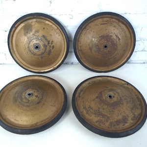 May include: A set of four circular metal wheels with a weathered gold finish and black rubber tires. Each wheel features a central hub with a visible axle opening, showing signs of oxidation and surface wear across the metallic surfaces.