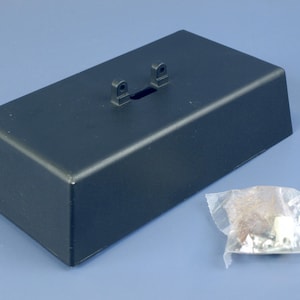 Può includere: Una base rettangolare grigio scuro con una piccola apertura e due staffe rialzate. Accanto alla base c'è un piccolo sacchetto di plastica contenente l'hardware. La base è probabilmente per un display o un montaggio.