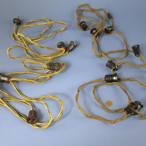 Puede incluir: Varios juegos de cableado eléctrico vintage con enchufes negros y cables trenzados amarillos y marrones. Los cables están dispuestos en bucles y conectados a enchufes. Se ve una moneda en uno de los bucles.