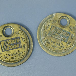 May include: Two vintage brass spark plug gap gauges with the "Auto Zone" logo and inch measurements. Each gauge has a circular design with a hole at the top and a scale for measuring gaps from .020 to .080 inches.