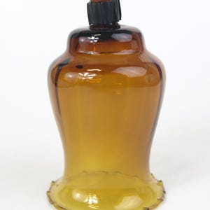 Puede incluir: Un portavelas de cristal color &aacute;mbar transl&uacute;cido con una base acampanada y festoneada y un cuerpo liso y redondeado. La abertura superior presenta una junta de goma estriada de color marr&oacute;n oscuro centrada en el borde de cristal.