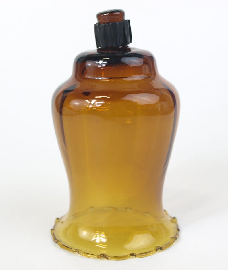 Puede incluir: Un portavelas de cristal color &aacute;mbar transl&uacute;cido con una base acampanada y festoneada y un cuerpo liso y redondeado. La abertura superior presenta una junta de goma estriada de color marr&oacute;n oscuro centrada en el borde de cristal.