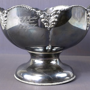 Puede incluir: Un bol de servir de plata con un borde festoneado y una base de pedestal. El bol tiene una inscripción que dice "To W.R. Butler, J. Ashworth, Fred. Brown, C.S. French."