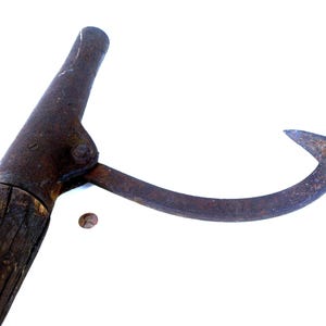 Puede incluir: Una antigua herramienta de gancho de metal oxidado con un mango de madera. El gancho es curvo y puntiagudo, y el mango es de color marrón oscuro. La herramienta parece vieja y usada, con signos de desgaste.