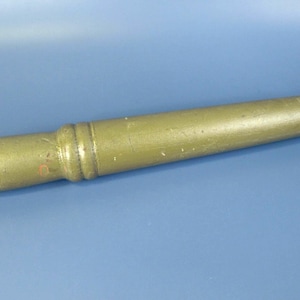 May include: A vintage, olive green wooden tool with a cylindrical body and a handle-like end. The tool has a slightly worn appearance, suggesting age and use. The other end has a small, square-shaped protrusion. The background is a solid blue.