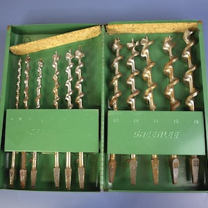 May include: A green metal drill bit set, open to reveal multiple drill bits. The set is labelled "Greenlee". The drill bits are silver and brown, and the lid has a cork lining. The sizes are marked.