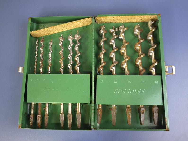 May include: Open green metal drill bit set with multiple drill bits of varying sizes. The set is labeled "Greenlee" and has a cork lining in the lid. The drill bits are silver and brown.