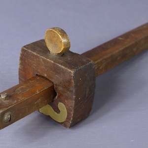 Puede incluir: Una herramienta de madera con un acento de latón, utilizada para marcar círculos. La herramienta tiene un mango y un brazo giratorio con una perilla de latón.