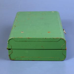 May include: A vintage green metal box with a hinged lid and a clasp closure. The box has rounded corners and shows signs of age with some rust spots. The overall design is simple and utilitarian.