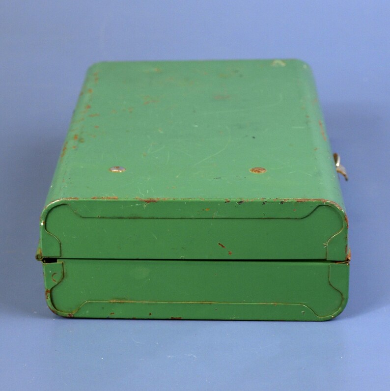 May include: A vintage green metal box with a hinged lid and a clasp closure. The box has rounded corners and shows signs of age with some rust spots. The overall design is simple and utilitarian.