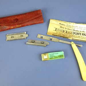 Może przedstawiać: Antyczny zestaw Durham-Duplex Safe Razor, w tym prostej maszynki do golenia z żółtą rączką, elementy ostrza, skórzane etui i opakowanie ostrzy. Zestaw zawiera instrukcje.
