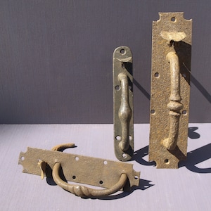 Könnte beinhalten: Vier antike Türklinken aus Metall mit rustikalem Finish. Die Griffe sind in verschiedenen Stilen und Größen, einige mit aufwendigen Details.