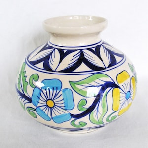 May include: A round ceramic vase with a cream-colored base featuring hand-painted floral patterns in blue, yellow, and green. The design includes a dark blue leaf motif around the neck and a wide, bulbous body with a short, flared rim opening.