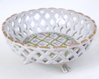 Puede incluir: Un cuenco de porcelana blanca con un diseño tejido y un patrón floral en el fondo. El cuenco tiene tres patas y es perfecto para servir fruta o aperitivos.