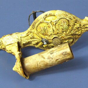 May include: Ornate, antique yellow and gold wall-mounted candle holder. The candle holder features detailed floral and scrollwork designs. The cylindrical candle holder is made of a light-colored material. A decorative piece for home decor.