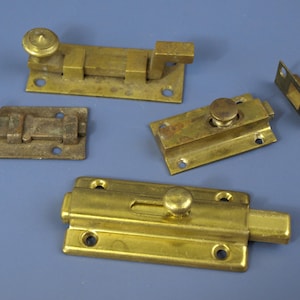 Puede incluir: Una variedad de pestillos y cerrojos de latón antiguos, en varios tamaños y diseños. Las piezas muestran signos de desgaste y envejecimiento. El fondo es azul liso.