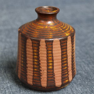 Könnte beinhalten: Eine kleine, braune Keramikvase mit einem gestreiften Muster in Braun-, Orange- und Gelbtönen. Die Vase hat einen runden Körper und einen schmalen Hals.