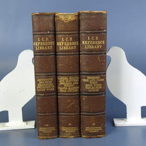 Puede incluir: Tres libros antiguos encuadernados en cuero marrón de la Biblioteca de Referencia I.C.S., con letras doradas. Los títulos incluyen "Aritmética, Dibujo, Instrumentos de Medición, Trabajo de Torno", "Cepilladoras, Formadoras y Ranuradoras, Taladrado y Mandrinado, Fresadora, Corte de Engranajes", y "Rectificado, Tornillo de Banco y Trabajo de Suelo, Consejos de Taller, Fabricación de Herramientas, Calibradores".