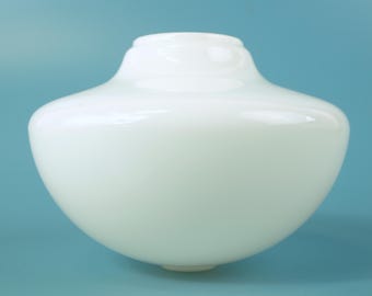 Puede incluir: Una pantalla de lámpara de vidrio blanco opaco y liso con un cuerpo redondeado y abombado, y una abertura circular más estrecha en la parte superior. La superficie del vidrio es brillante y refleja la luz, creando un aspecto limpio y uniforme.