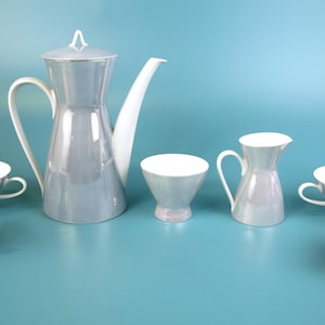 May include: A vintage tea set in grey and white. It features a coffee pot, creamer, sugar bowl, and six teacups. The teacups have a rounded design and a small handle. The set is made of porcelain, a classic design.