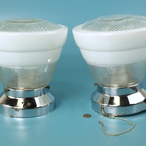 May include: Two vintage light fixtures with white glass shades and chrome bases. The shades have a clear, textured glass top and a ribbed glass lower section. The fixtures are on a blue background.