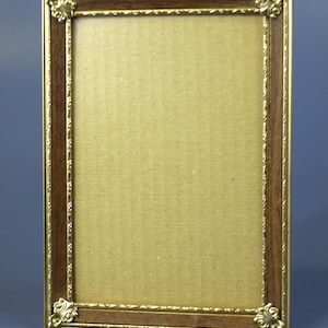 May include: A rectangular picture frame with a gold-coloured border and a dark brown wooden interior. The frame has decorative corner accents and a cardboard backing. The frame is designed to hold a photograph or artwork.