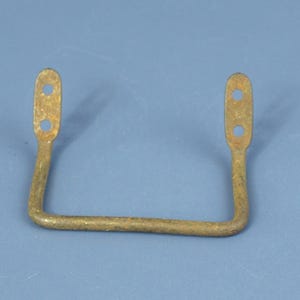 May include: A vintage, U-shaped metal handle with a weathered, golden-brown finish. Each end features an elongated section with two circular holes. The handle's design suggests it may be from an antique piece of furniture or hardware.
