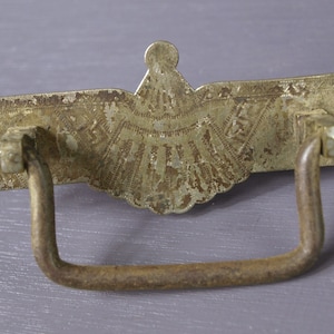 May include: A vintage, ornate, silver-toned metal drawer pull with a decorative, scalloped design and a simple, curved metal handle.