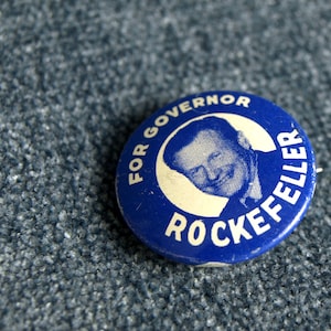 May include: A blue and white campaign button with the text "For Governor Rockefeller" and a black and white image of a man's face.