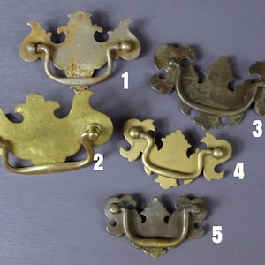 May include: Five antique brass drawer pulls with ornate designs. The pulls are numbered 1 through 5.