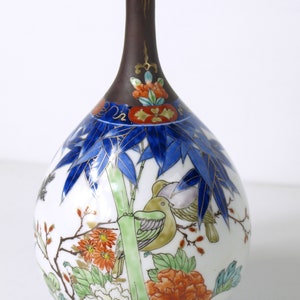Op de afbeelding: Een witte porseleinen vaas met een bruine hals en een bloemenmotief. De vaas is versierd met blauwe, groene en rode bloemen, evenals twee vogels.