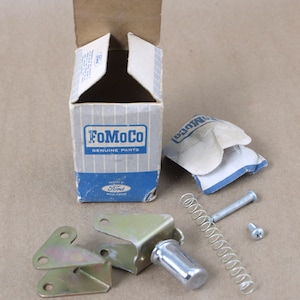 Könnte beinhalten: Eine Vintage-Ford FoMoCo Genuine Parts Box mit einem Metallschalter, einer Feder und zwei Schrauben. Die Box ist blau und weiß mit dem Ford-Logo und den Worten "FoMoCo Genuine Parts".