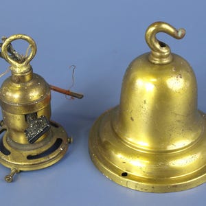 May include: A brass light fixture component with a black turn-key switch and a separate brass bell-shaped canopy featuring a top hook. Both items exhibit a metallic gold finish with visible signs of wear and patina on their surfaces.