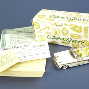 May include: A white and brown toy convertible car with yellow interior, next to a box and paperwork. The box is white with gold accents and the words "Collector's Classics". The car has the words "Desoto Pace Car" on the side.