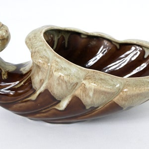May include: A brown and white ceramic cornucopia planter with a curled handle. The planter has a glazed finish and a rustic look.