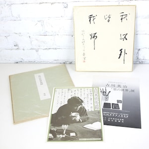 Puede incluir: Colección de libros y efímeras japonesas, que incluye una caja con caligrafía, un libro con una etiqueta blanca y una foto en blanco y negro de una persona. Los artículos están dispuestos sobre una superficie blanca.