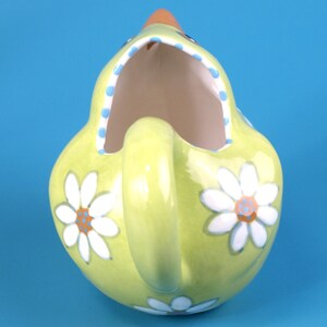 Puede incluir: Jarra de cer&aacute;mica verde claro con asa, con forma de gallina. Decorada con margaritas blancas y un borde de lunares azules. El pico es naranja. Ideal para servir bebidas.